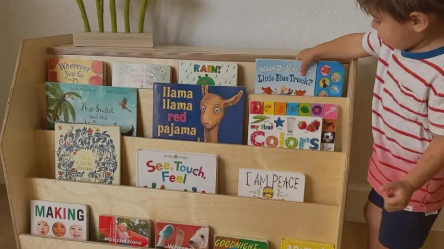 Little boy picking out a book from a Montessori bookshelf