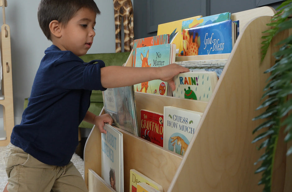 boy picking up a book from the front facing montessori bookshelf