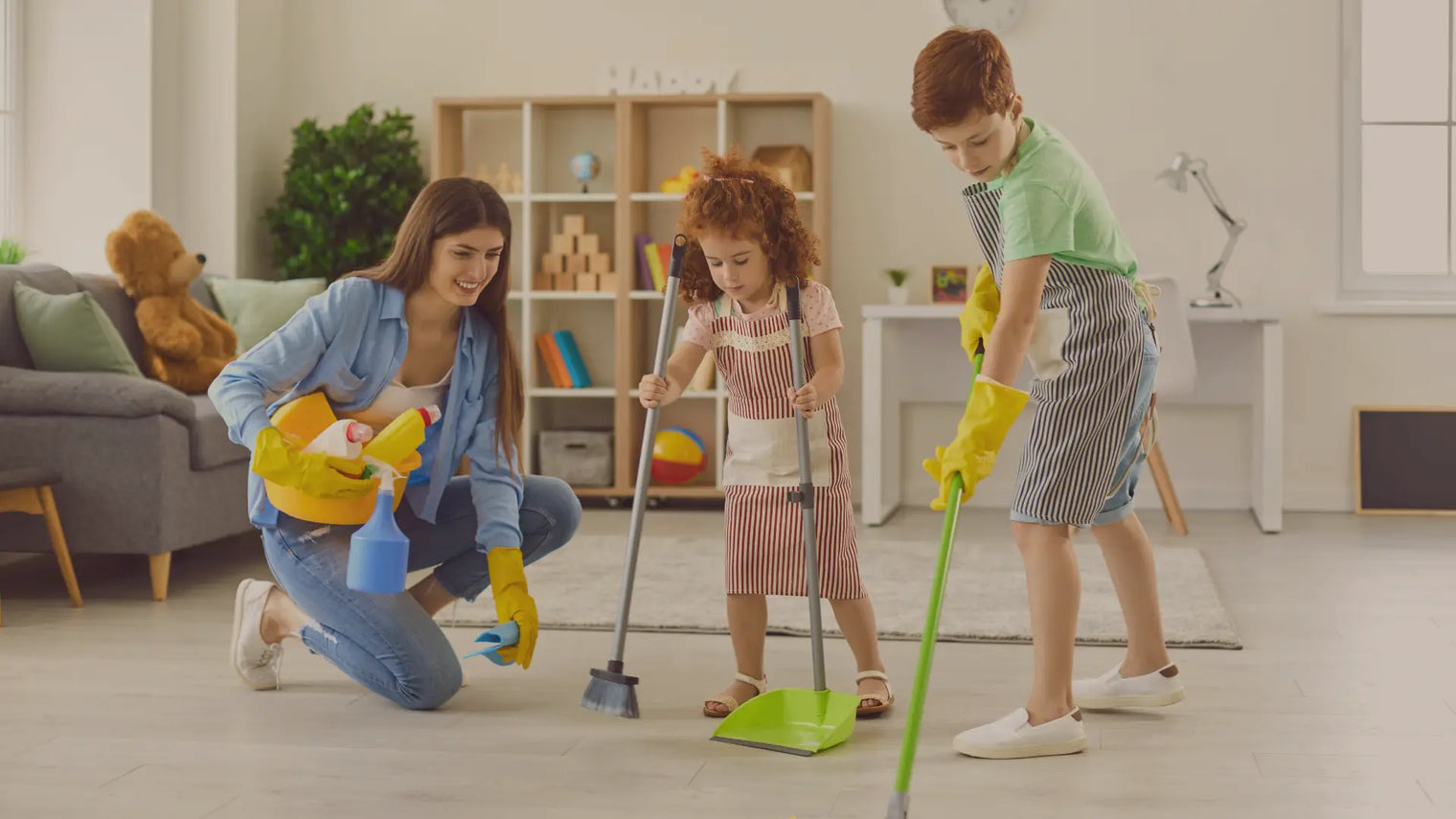 A little girl and her older brother sweeping the floor with their mom.