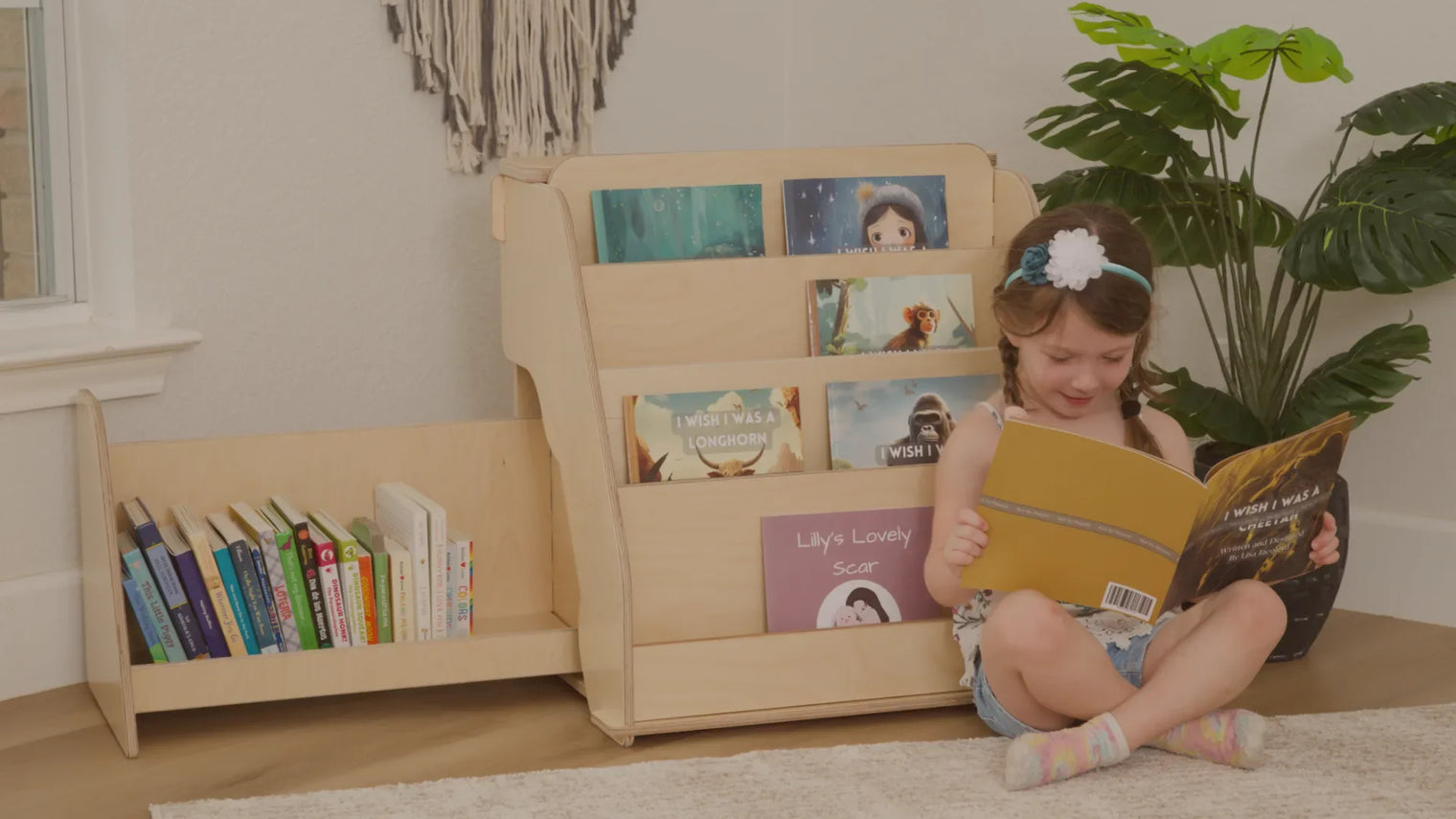 A little girl reading a book next to a small Montessori bookshelf