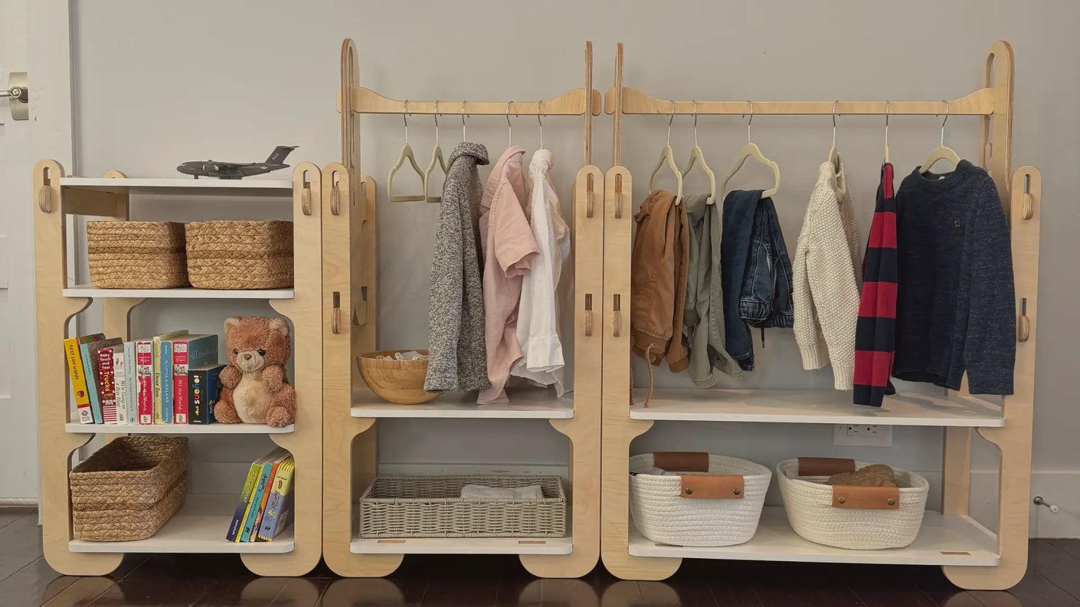 A Montessori children's wardrobe set with hanging clothes, organizational baskets, and books/toys.
