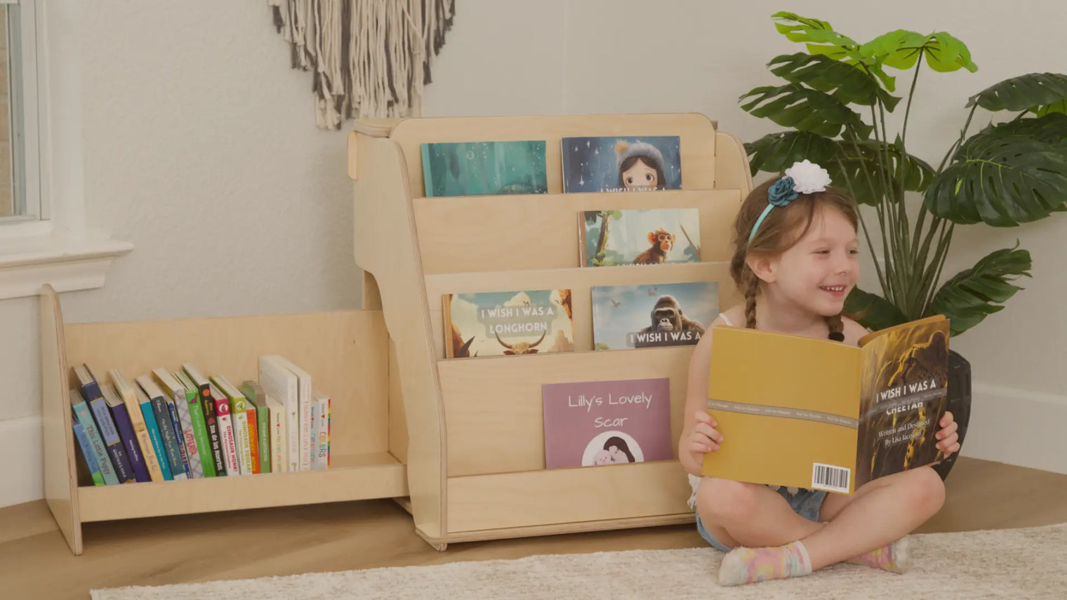 Little girl reading a book in front of a Montessori bookshelf for toddlers with hidden storage created by Dannico.