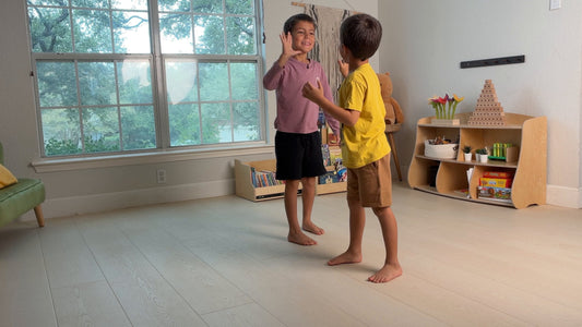 Two boys high-five in a tidy playroom after resetting a Dannico front-facing bookshelf and Joy Shelf toy shelf