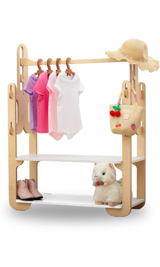 Handcrafted 30-inch wooden clothing rack, featuring a variety of children's clothing and accessories. The rack holds vibrant purple, pink, and white T-shirts on natural wood hangers. A woven straw hat with a multicolored band adorns the top shelf, alongside a playful straw basket embellished with fruit motifs. A pair of chic pink toddler boots and a plush llama toy with a colorful necklace grace the bottom shelf. Perfect for organizing and displaying kids' fashion