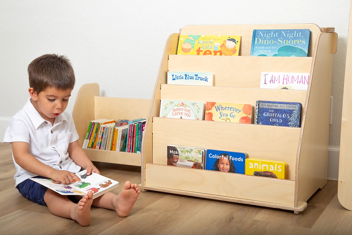 Little boy reading a book next to Montessori bookshelf