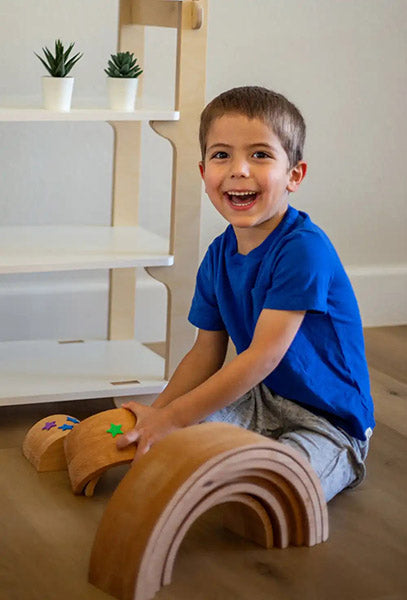 happy boy playing with his montessori toy in front of montessori shelf