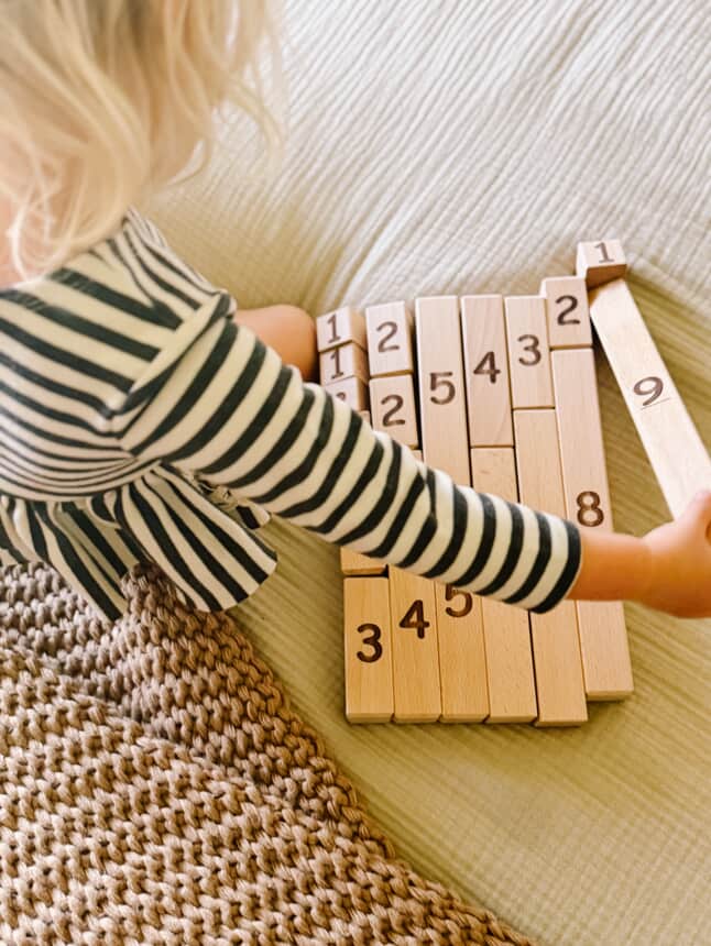 Child playing with wooden number blocks horizontally on bed