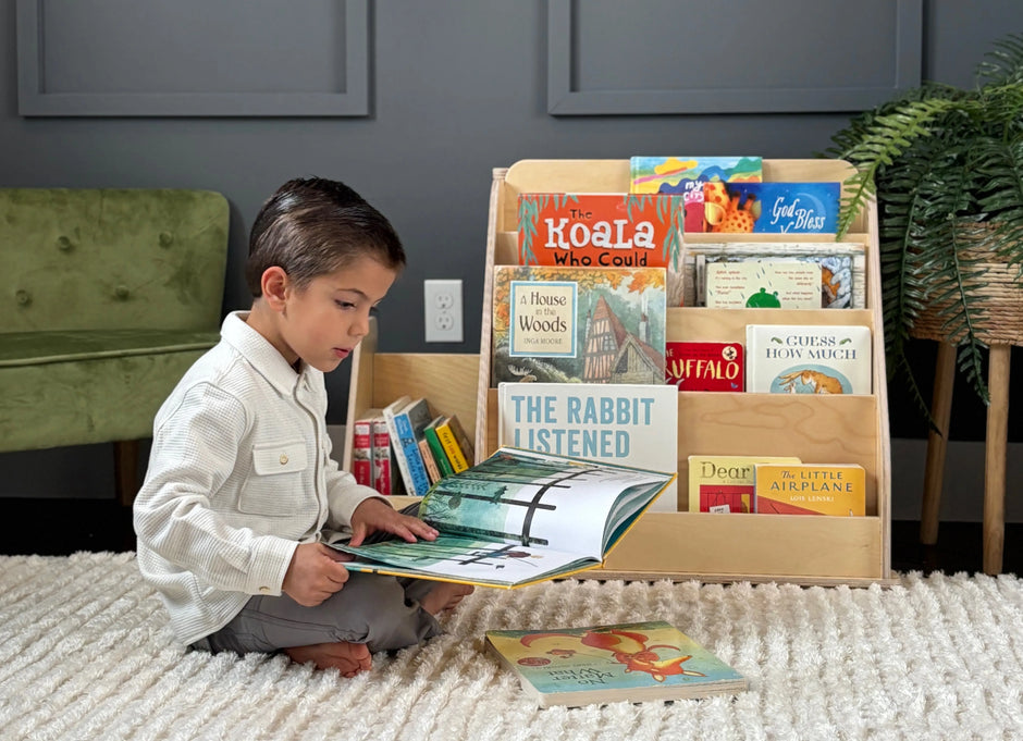 little boy reading a book in front of the Montessori bookshelf