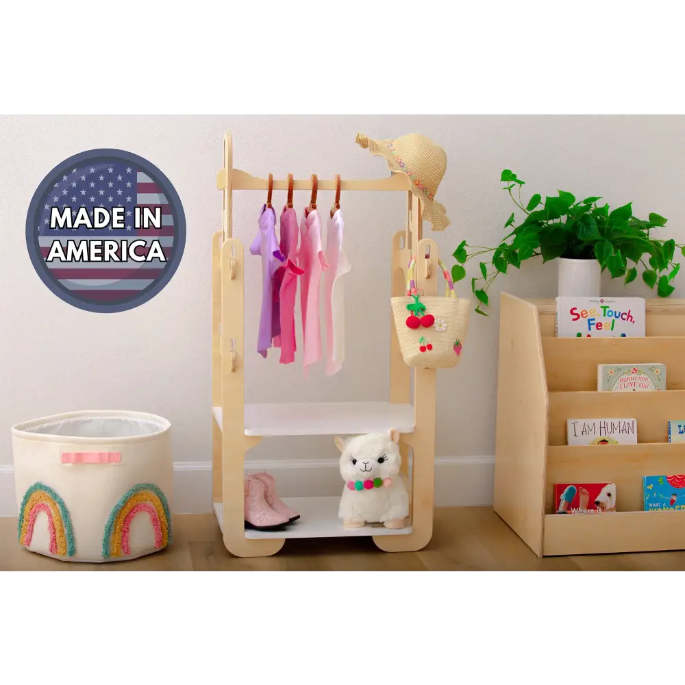 Locally-crafted 'Made in America' wooden clothing rack for kids by Dannico Woodworks, showcasing a straw hat, colorful clothes, and a woven basket, set against a nursery backdrop with educational toys and books.