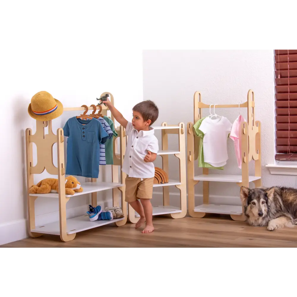 Boy playing with toy dinosaur next to stylish wooden clothes racks filled with children's clothes and accessories, accompanied by a friendly dog