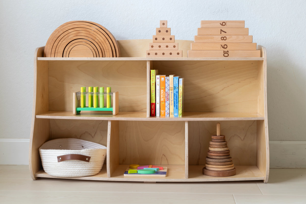 Montessori toy shelf organized with books, stacking rings, abacus, and a woven basket